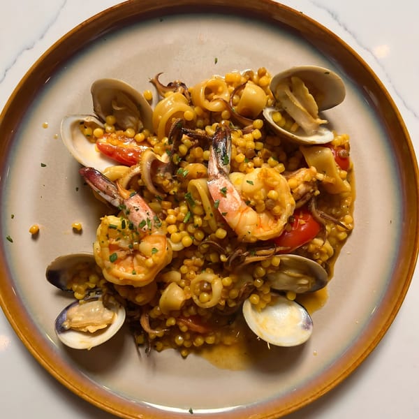 Italian seafood pasta with shrimp, clams, squid, and cherry tomatoes on a light brown plate.