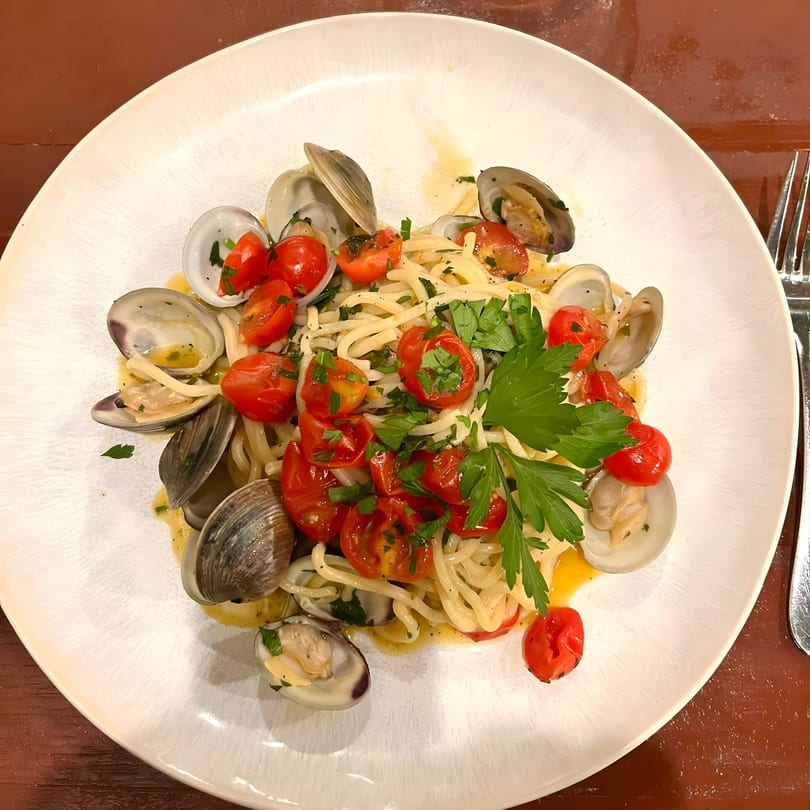 Tre Monti's linguine alle vongole with fresh clams, cherry tomatoes, and parsley on a white plate.